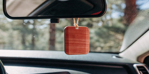 A long lasting natural wood car air freshener hanging from a rearview mirror.