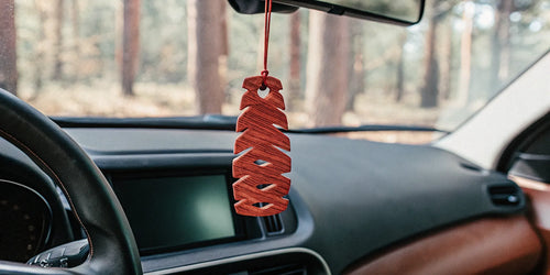 A wood car air freshener from a monthly box hanging on a car's rearview mirror.