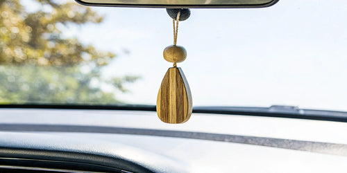 A wood car air freshener that lasts, hanging from a rearview mirror.