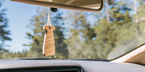 A wooden reusable car air freshener hanging from a rearview mirror.