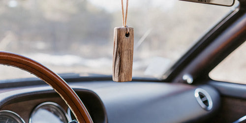 A Drift wood car freshener hanging from a car's rearview mirror.