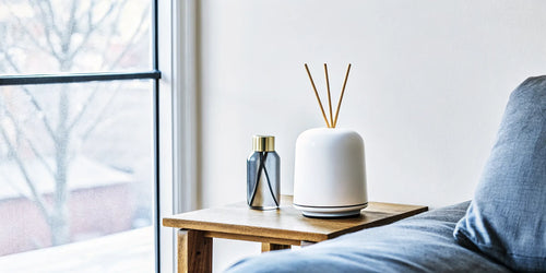 Modern living room with a minimalist white electric scent diffuser on a side table and a glass reed diffuser on a shelf, Scandinavian interior design
