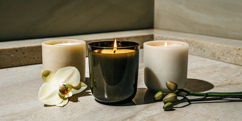 A vanilla scented candle burning next to a white orchid for a relaxing ambiance.