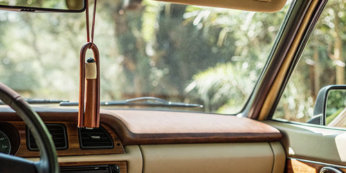 A mahogany teakwood car air freshener refill hanging from a rearview mirror.