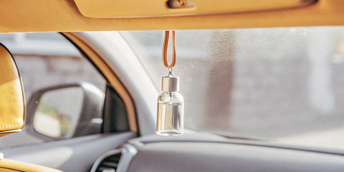 Car air freshener diffuser bottle hanging from a rearview mirror.
