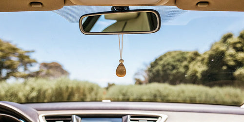 Teak car air freshener hanging from a car's rearview mirror.
